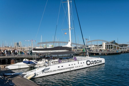 Large catamaran docked at a marina with people on the boardwalk and clear sky.