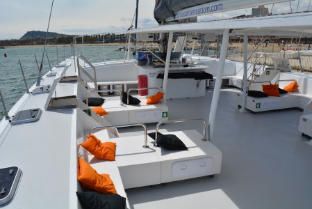 White yacht deck with orange and black cushions, overlooking a coastline.