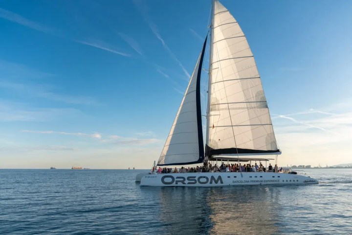 Sailing catamaran with people onboard on calm sea at sunset.